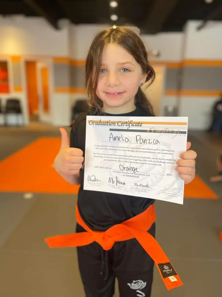 Child earning belt stripe at Mastery Martial Arts Troy MI, proud moment with instructor