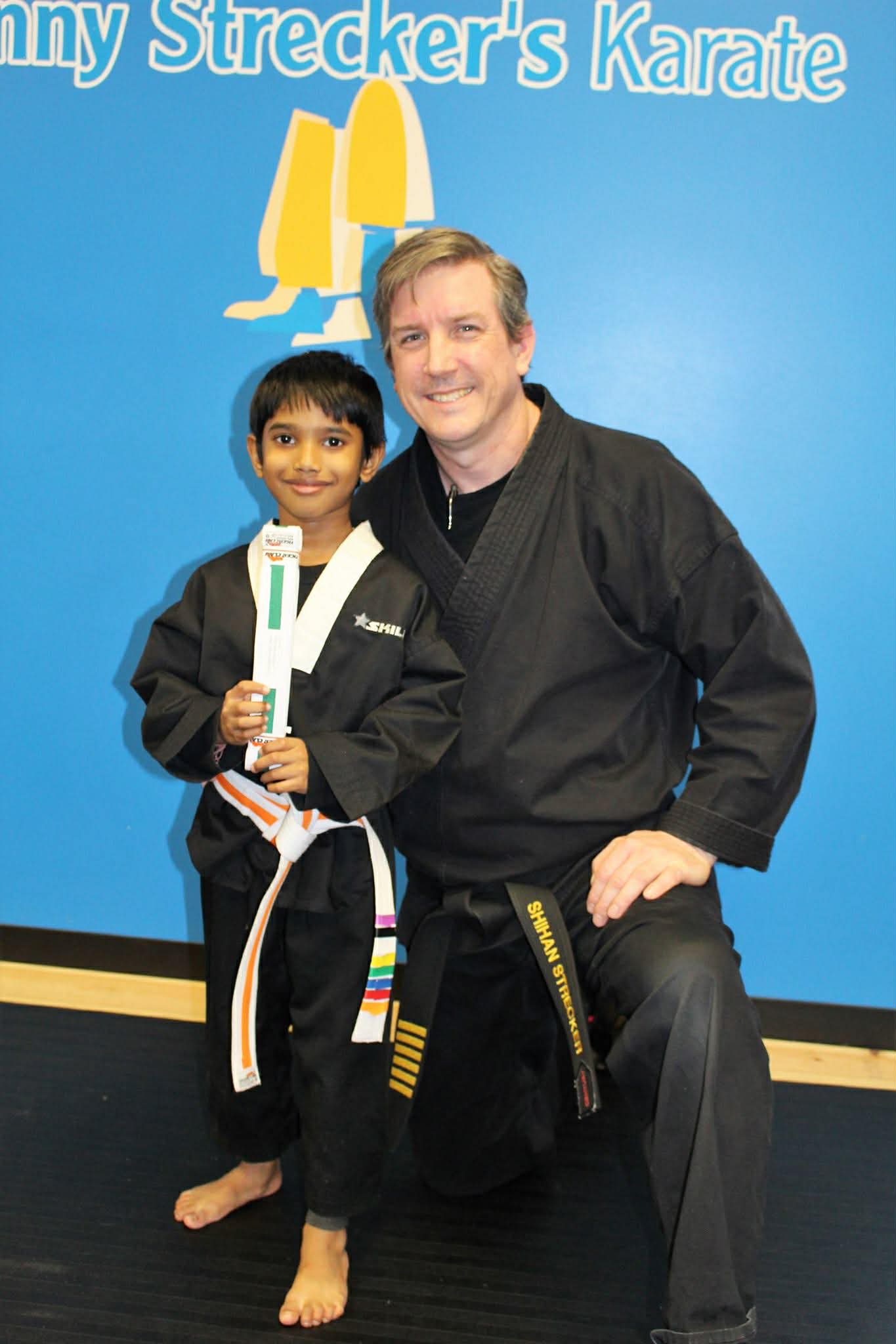 Anay Pai posing with Instructor Denny Strecker at Denny Strecker's Karate, holding his belt certificate
