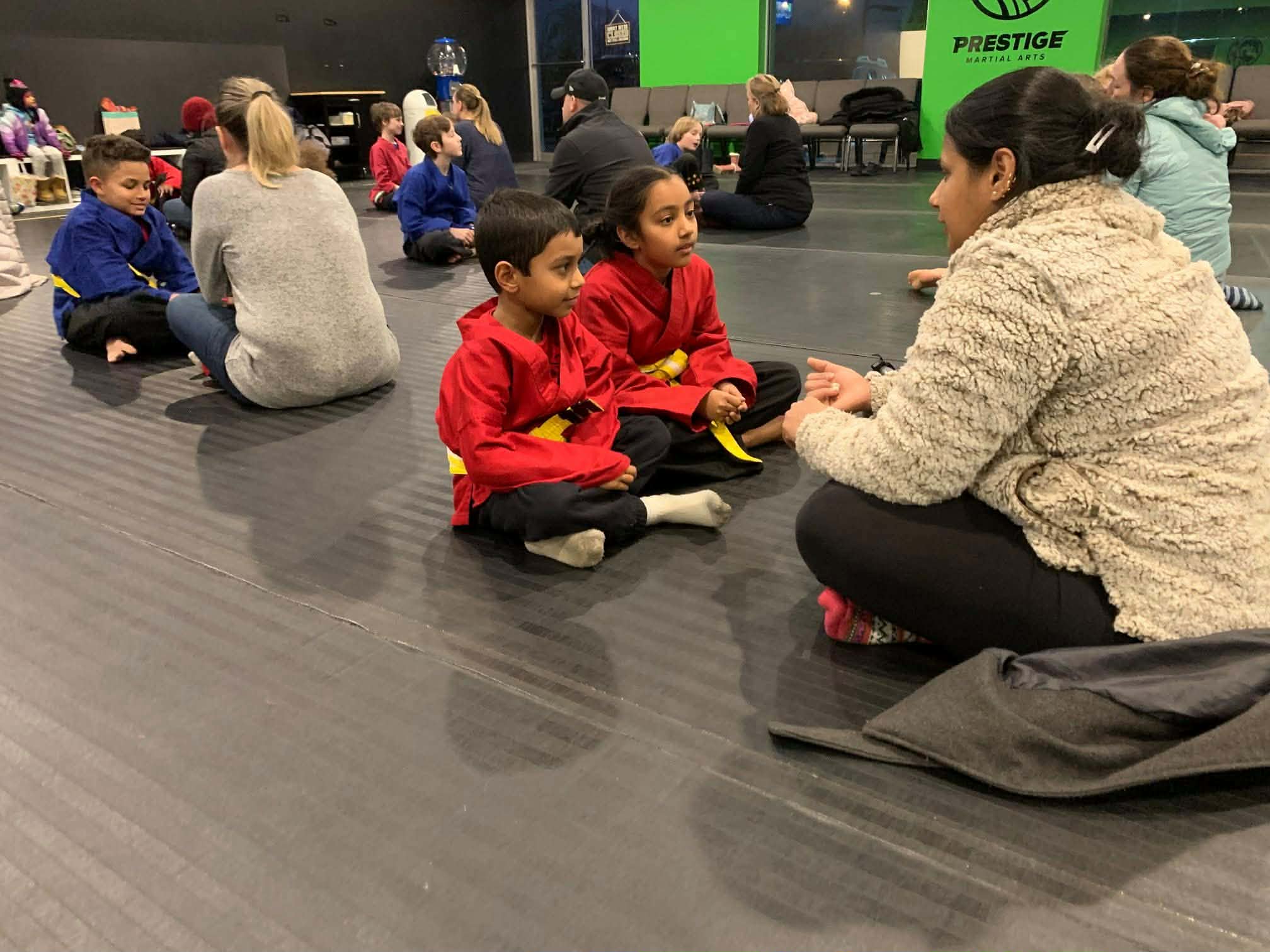 Nishi Bergi sitting on the mat with her brother and mom during a martial arts class