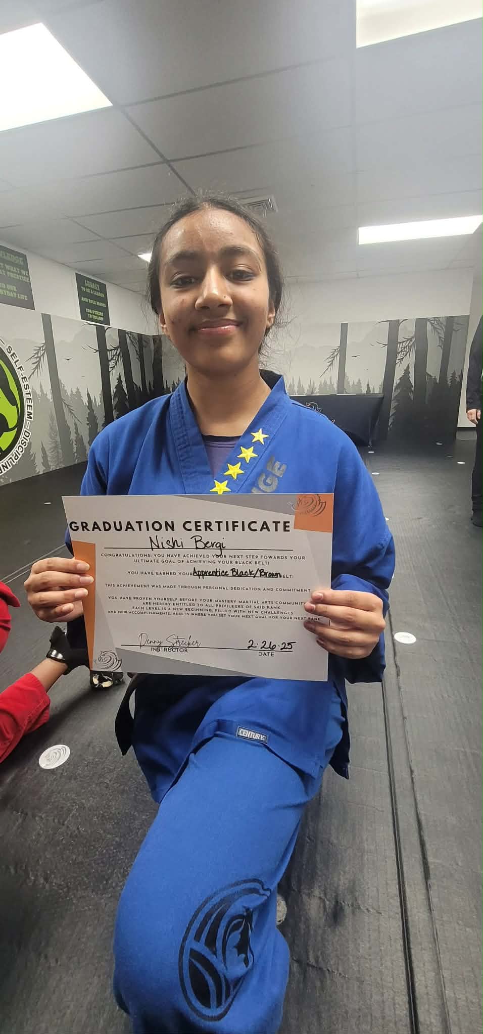 Nishi Bergi holding her Apprentice Black/Brown Belt graduation certificate signed by Instructor Denny Strecker