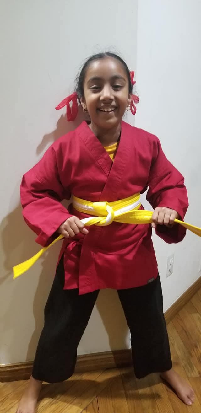 Nishi Bergi in her red uniform proudly showing off her yellow belt — an early milestone on her journey to black belt