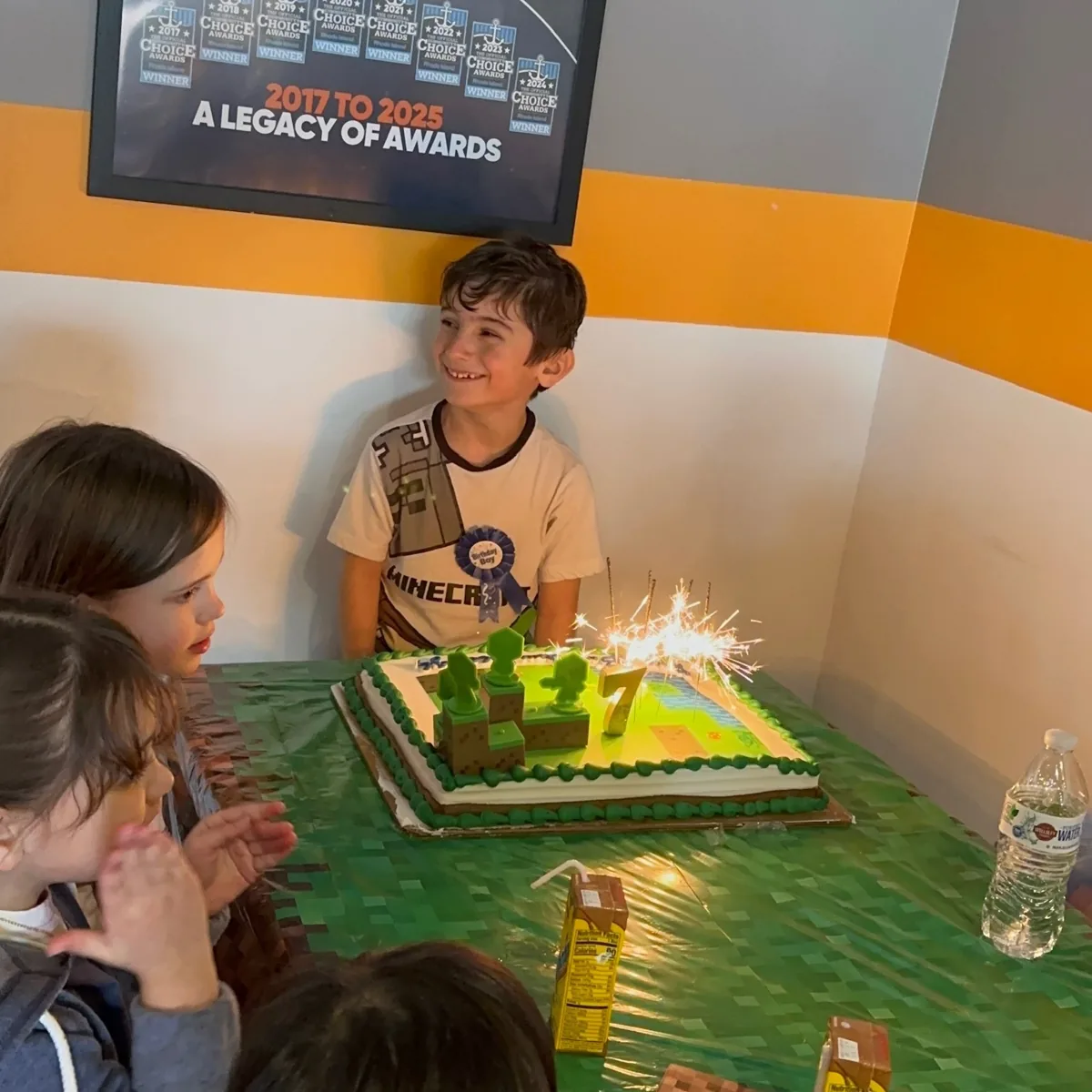 Birthday boy behind his sparkler-lit cake surrounded by cheering friends